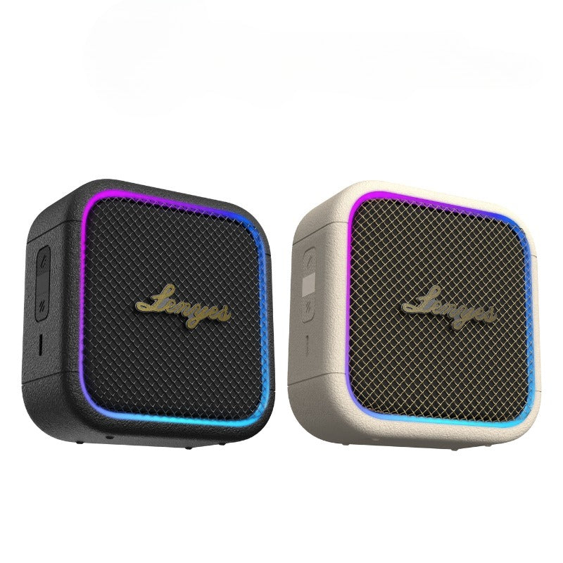 Two small square portable speakers shown side by side on a plain white background. The left speaker is black with a purple and blue LED light border and a gold-tone logo.