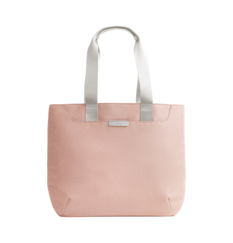 A light pink textured tote bag with light gray fabric shoulder straps and a small silver metal brand plaque on the front, shown against a plain white background.
